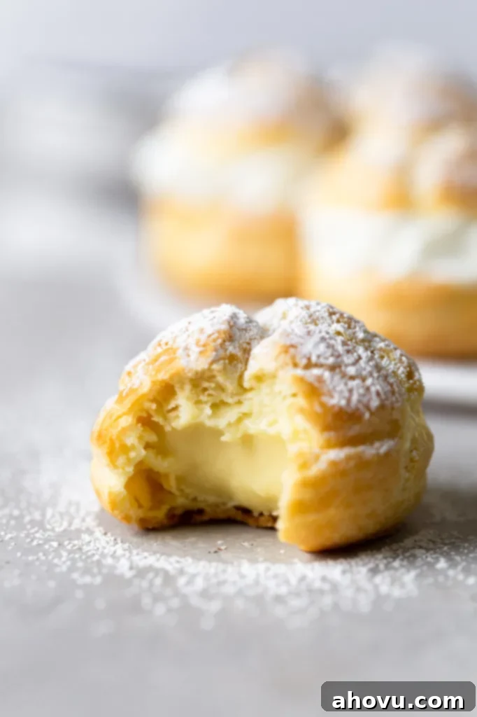 A cream puff with a bite missing. More filled cream puffs are on a plate in the background. 