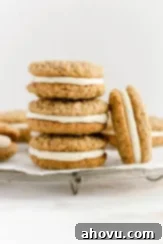 A stack of homemade oatmeal cream pies on a wire rack. One oatmeal cream pie is leaning up against the stack. Classic, soft, and creamy oatmeal pies.