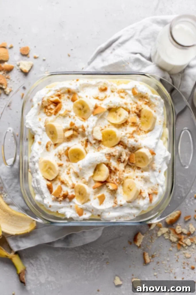 Overhead view of a baking dish filled with banana pudding from scratch. Crushed Nilla Wafers and a banana peel surround the baking dish. 
