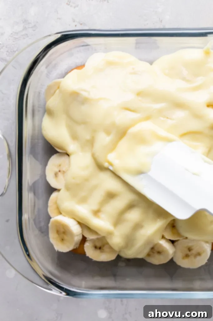 Overhead view of homemade vanilla pudding being spread over a layer of Nilla Wafers and banana slices. 