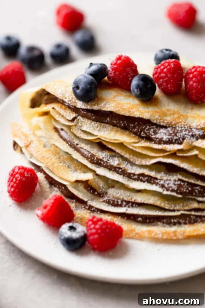 A stack of homemade crepes oozing Nutella and topped with fresh berries. More berries are scattered in the background. 
