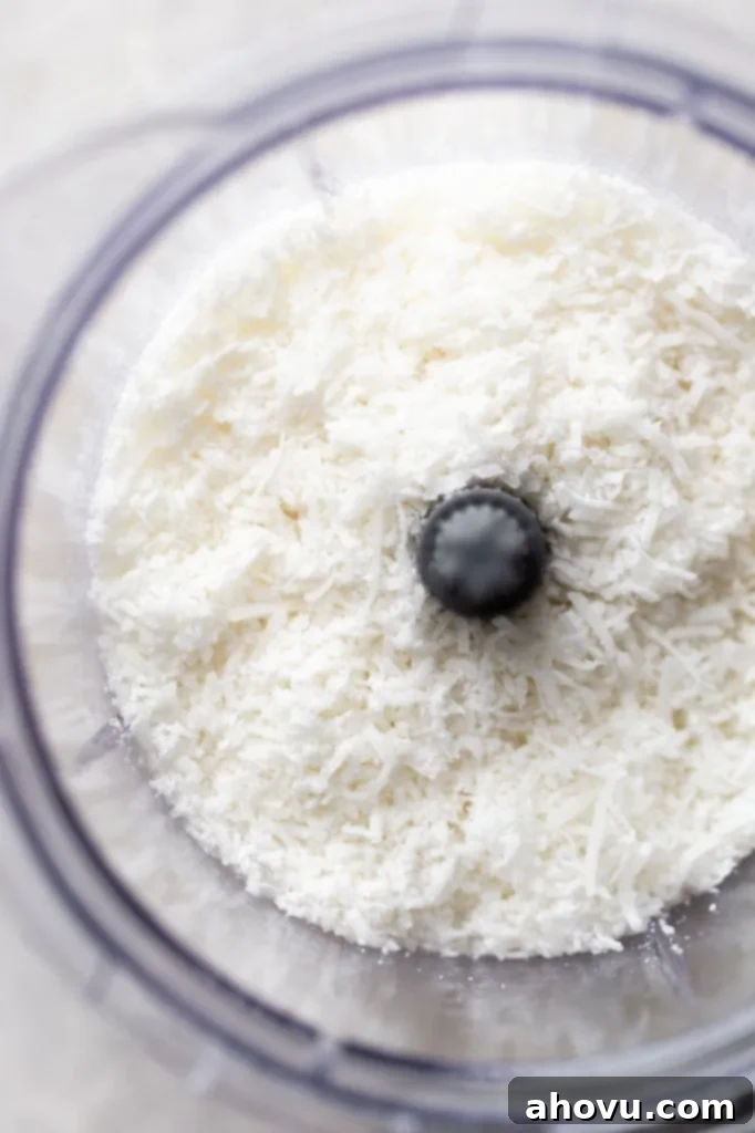 Overhead view of sweetened shredded coconut being pulsed in a food processor.