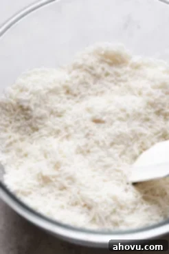Sweetened shredded coconut in a glass mixing bowl with a rubber spatula, ready for mixing.