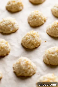 Baked coconut macaroons cooling on a parchment paper-lined baking sheet.