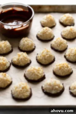 Chocolate dipped macaroons on a baking sheet next to a bowl of melted chocolate.
