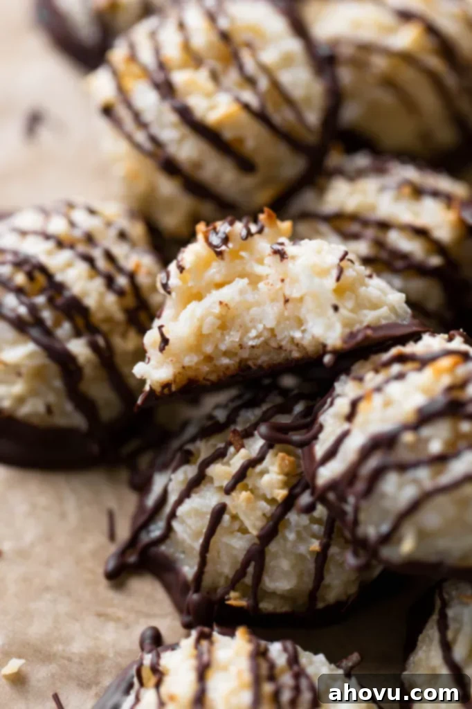 Close up view of a pile of chocolate dipped macaroon cookies. The top cookie has a bite missing, revealing the chewy interior.