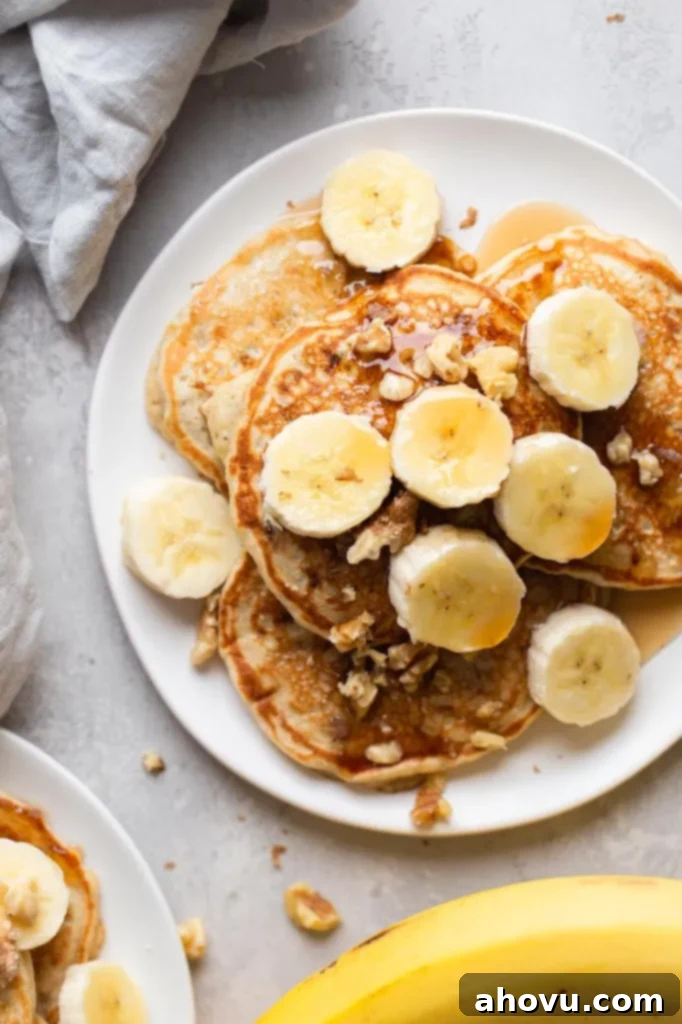 Overhead view of fluffy banana pancakes topped with banana slices and chopped walnuts on a white plate. 