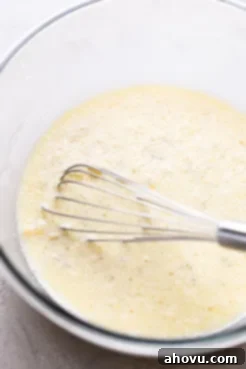 Wet pancake ingredients with a whisk in a glass mixing bowl.