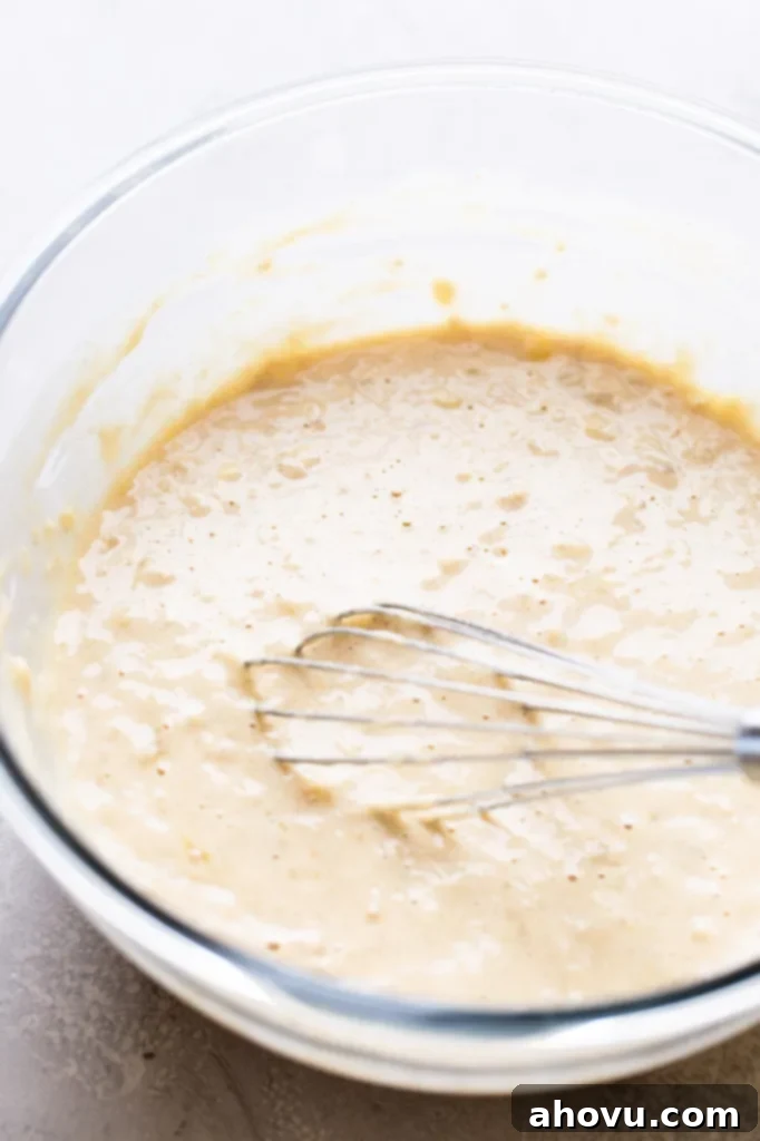 Homemade banana pancake batter with a whisk in a glass mixing bowl. 