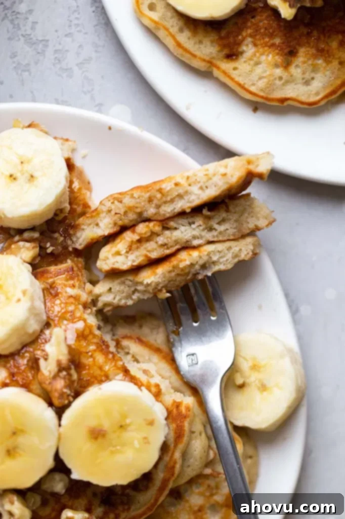 Overhead view of fluffy banana pancakes on a white plate. A fork has speared a bite of pancake. 