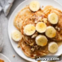 Overhead view of banana pancakes topped with banana slices and chopped walnuts on a white plate.