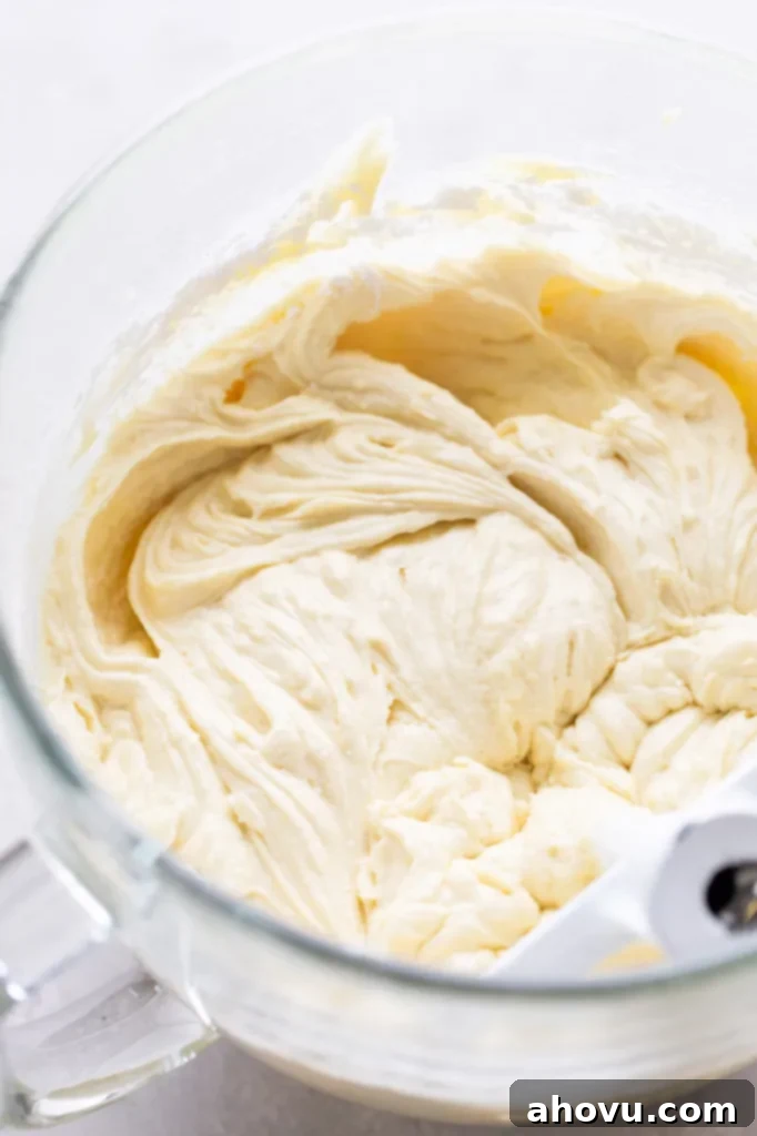 Smooth vanilla cake batter fills a clear glass mixing bowl, with the paddle attachment of a stand mixer resting gently within it, ready for baking.