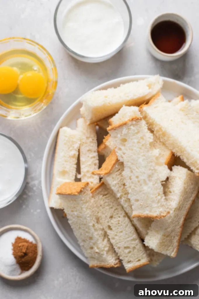 An overhead shot showcasing all the essential ingredients laid out for preparing homemade cinnamon French toast sticks, including slices of bread, fresh eggs, whole milk, heavy cream, vanilla extract, granulated sugar, and ground cinnamon.