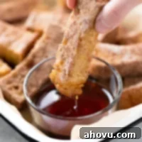 A delicious baked French toast stick being dipped into a small bowl of rich maple syrup, showcasing its golden color and cinnamon sugar coating, ready to be enjoyed.