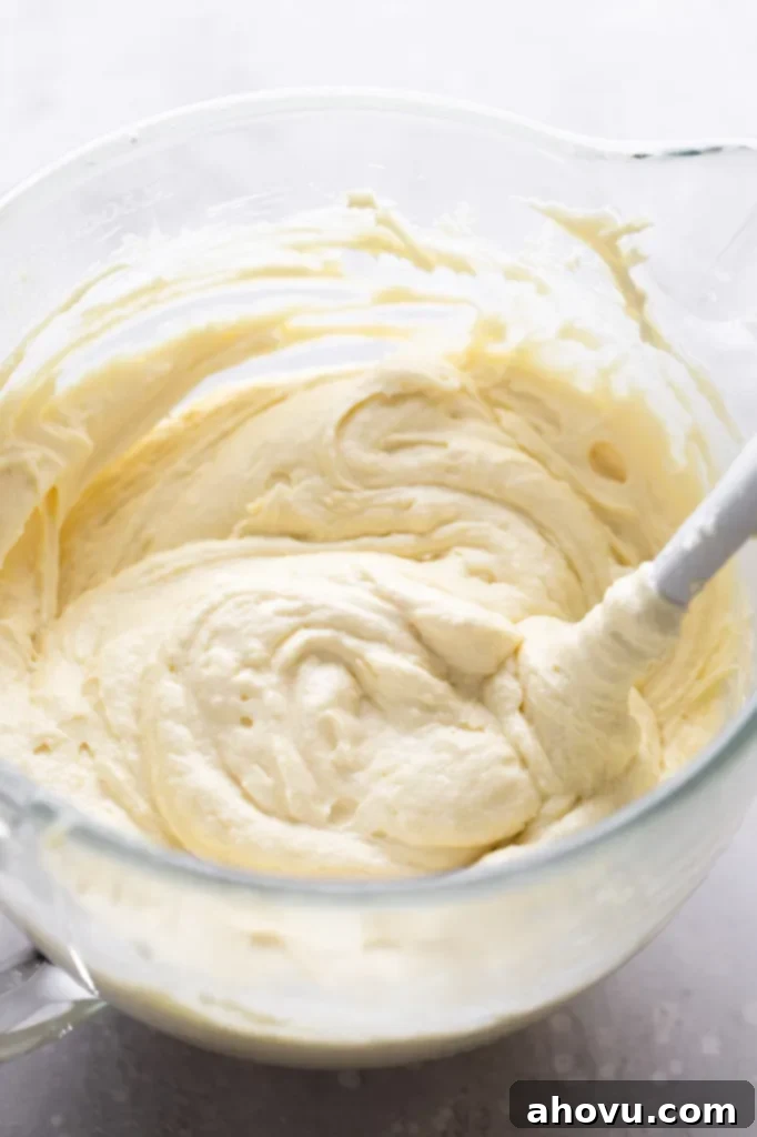 Vanilla cake batter in a glass mixing bowl with a rubber spatula. 