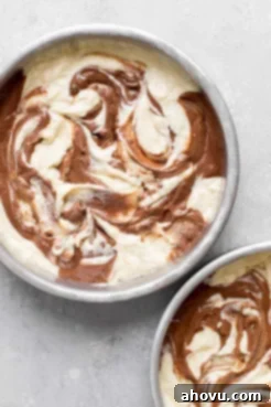 An overhead view of swirled marble cake batter in two cake pans, ready to be baked.