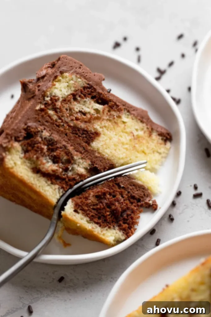 An overhead view of a slice of marble cake on a white plate. A fork is digging into the slice. 