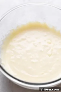 A clear glass mixing bowl filled with plain, creamy cake batter.