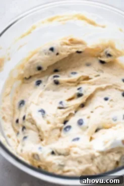 A glass mixing bowl filled with fluffy blueberry coffee cake batter, showing visible blueberries mixed in.