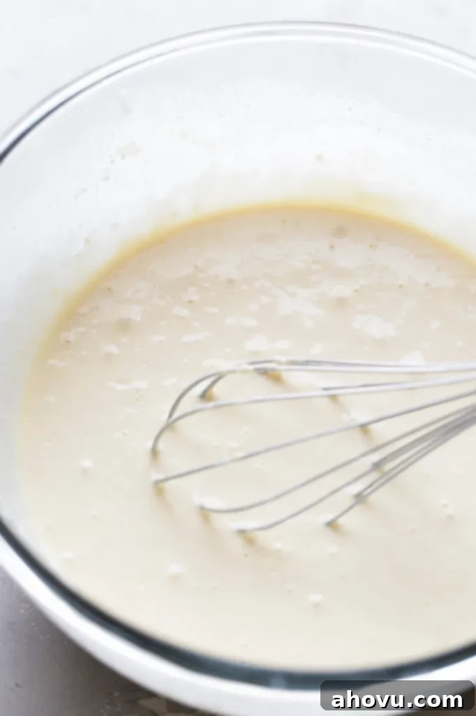 Waffle batter in a glass mixing bowl. A whisk rests in the mixing bowl. 