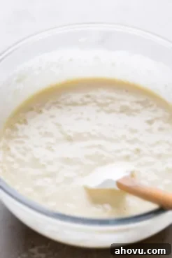A glass mixing bowl full of waffle batter. A rubber spatula rests in the bowl.