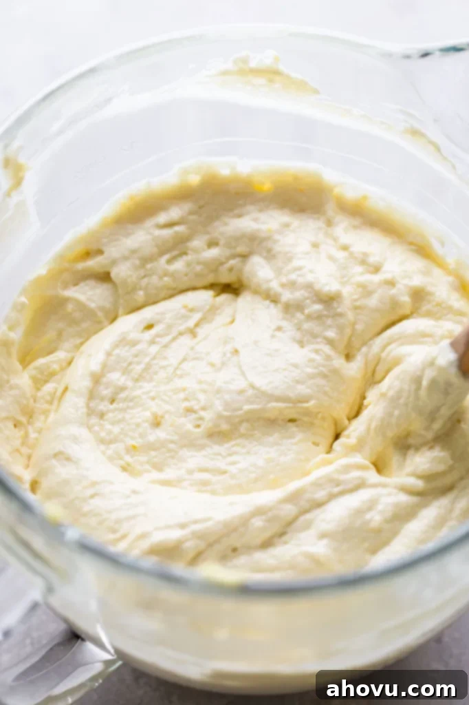 Homemade lemon cake batter in a glass mixing bowl. A wooden spoon rests in the bowl. 