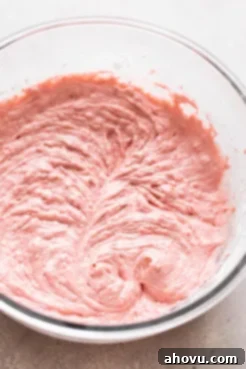 A close-up of light pink strawberry cupcake batter being mixed in a glass bowl, showcasing its smooth, creamy texture before baking.