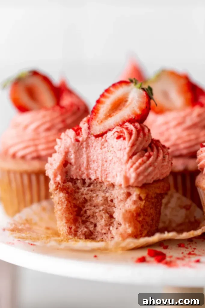 A delicious close-up view of frosted strawberry cupcakes on a cake stand, with one cupcake tantalizingly showing a bite missing, revealing its tender pink interior.