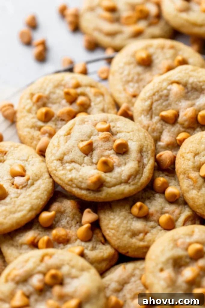 Golden Butterscotch Bites 5 A close up view of butterscotch chip cookies piled on a wire cooling rack. Additional butterscotch chips are scattered in the background.
