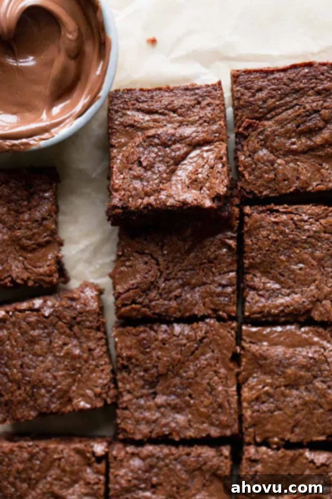 A close-up, overhead view of perfectly sliced Nutella brownies, displaying their rich, fudgy interior and the beautiful Nutella swirl, presented alongside a small bowl of Nutella.