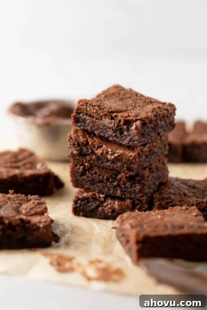 A delectable stack of four fudgy Nutella brownies, with more brownies scattered around, highlighting their perfect texture and rich appearance.
