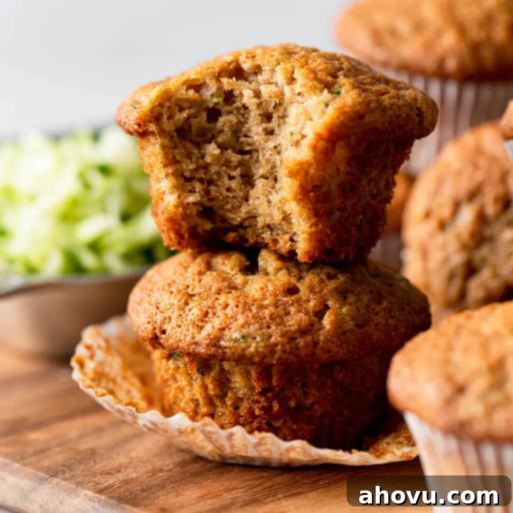 Two zucchini bread muffins stacked on top of each other. The top muffin has a bite missing. 