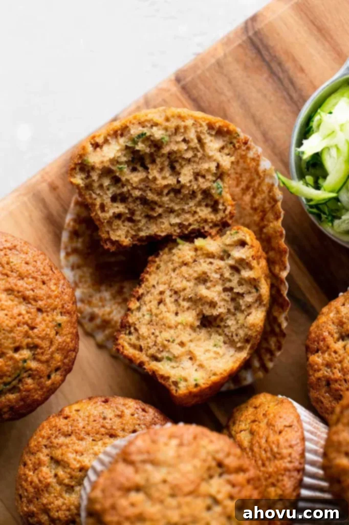 An overhead view of zucchini muffins on a wood cutting board. One muffin has been cut in half and others are lying on their sides. 