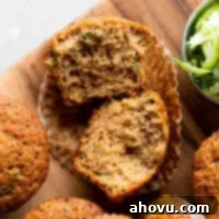 An overhead view of zucchini muffins on a wood cutting board. One muffin has been cut in half and others are lying on their sides.