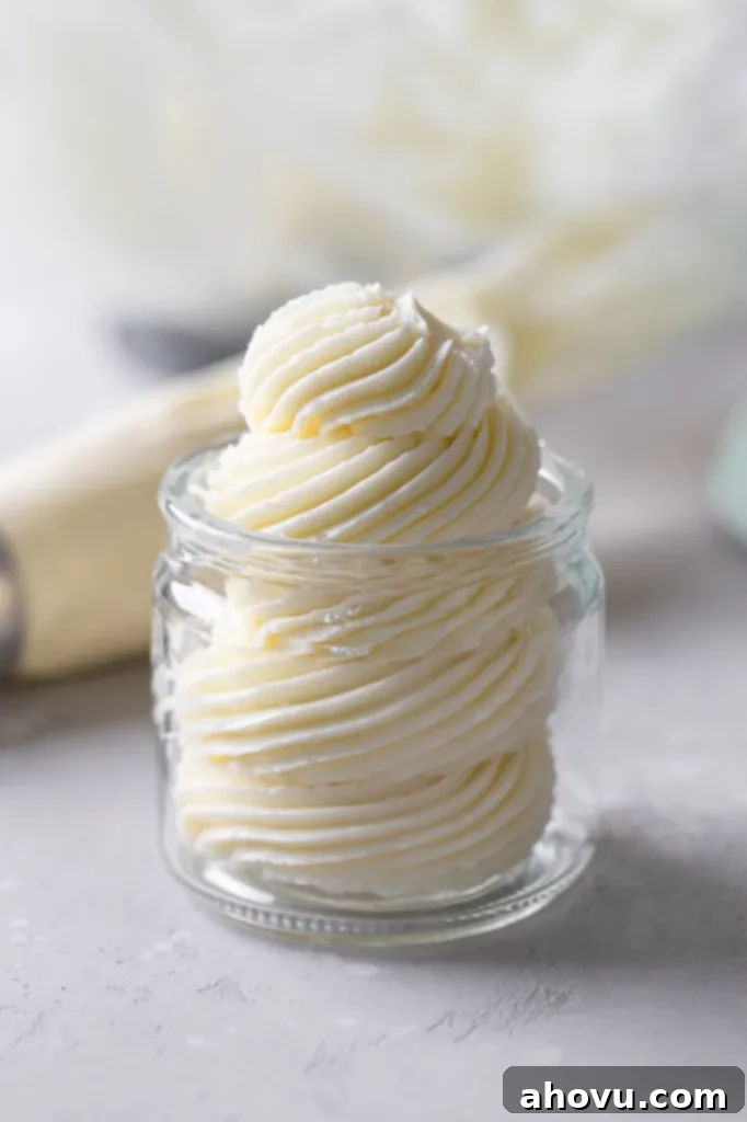 Swiss meringue buttercream frosting piped into a glass jar. A piping bag lies in the background. 