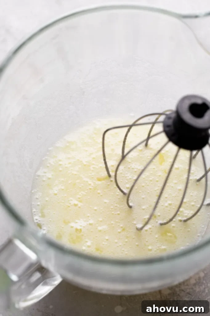 An overhead view of egg whites in a glass mixing bowl with a whisk. 