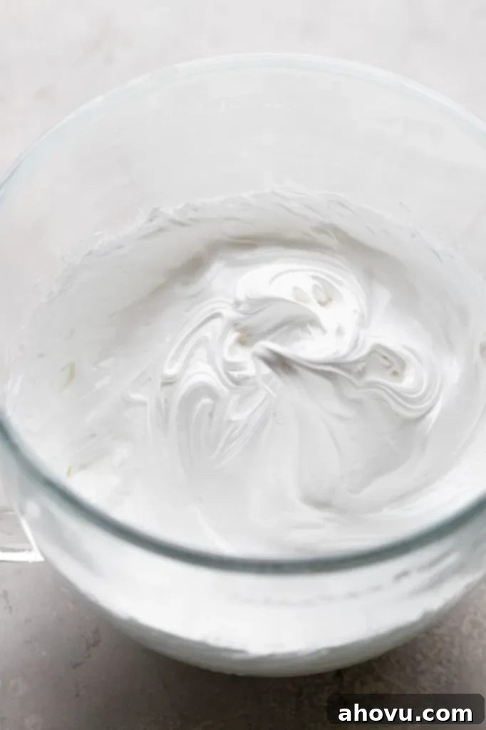 An overhead view of egg whites that have been whipped to stiff peaks in a glass mixing bowl. 