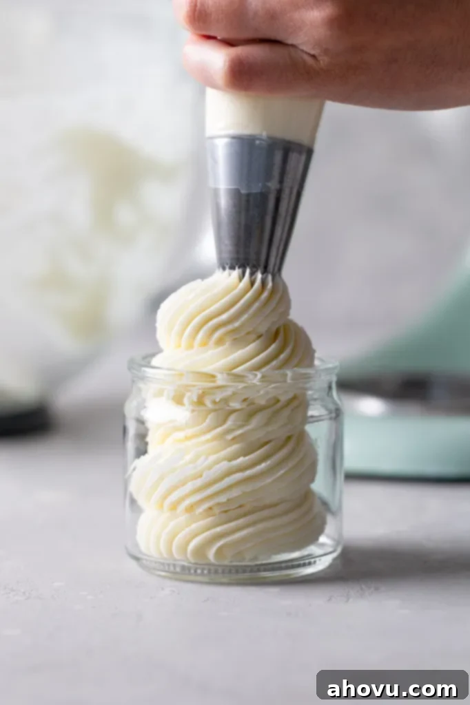 Swiss meringue buttercream being piped into a glass jar from a piping bag. 