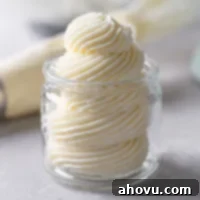 Swiss meringue buttercream frosting piped into a glass jar. A piping bag lies in the background.