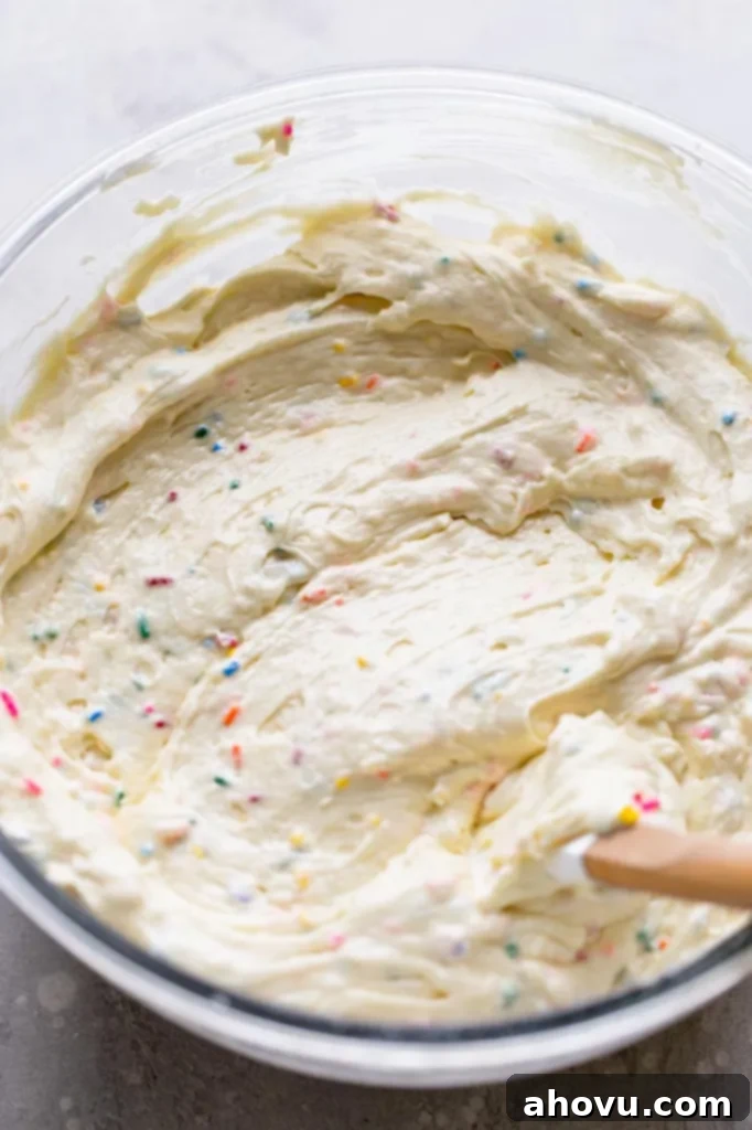 An overhead view of funfetti cake batter in a glass mixing bowl with a rubber spatula. 