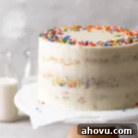 A homemade funfetti cake on a cake stand. Two glass bottles of milk are in the background.