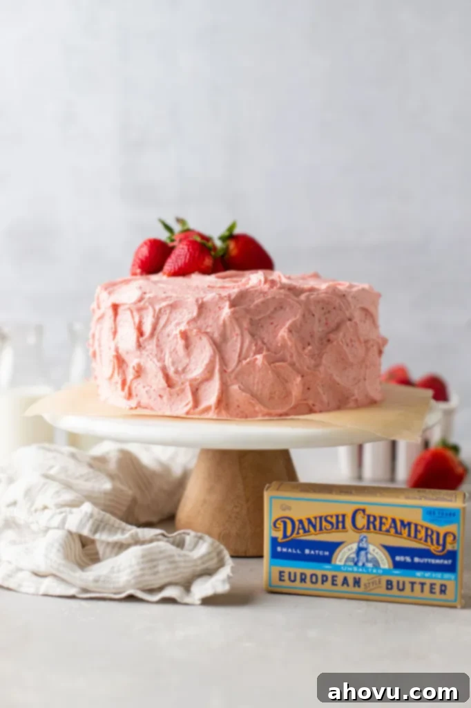 A beautifully frosted strawberry cake topped with fresh strawberries, displayed on a cake stand next to Danish Creamery butter and a napkin.