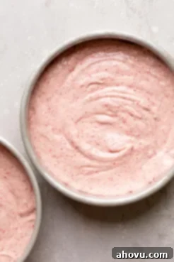 Smooth strawberry cake batter evenly poured into two round cake pans, ready for the oven.