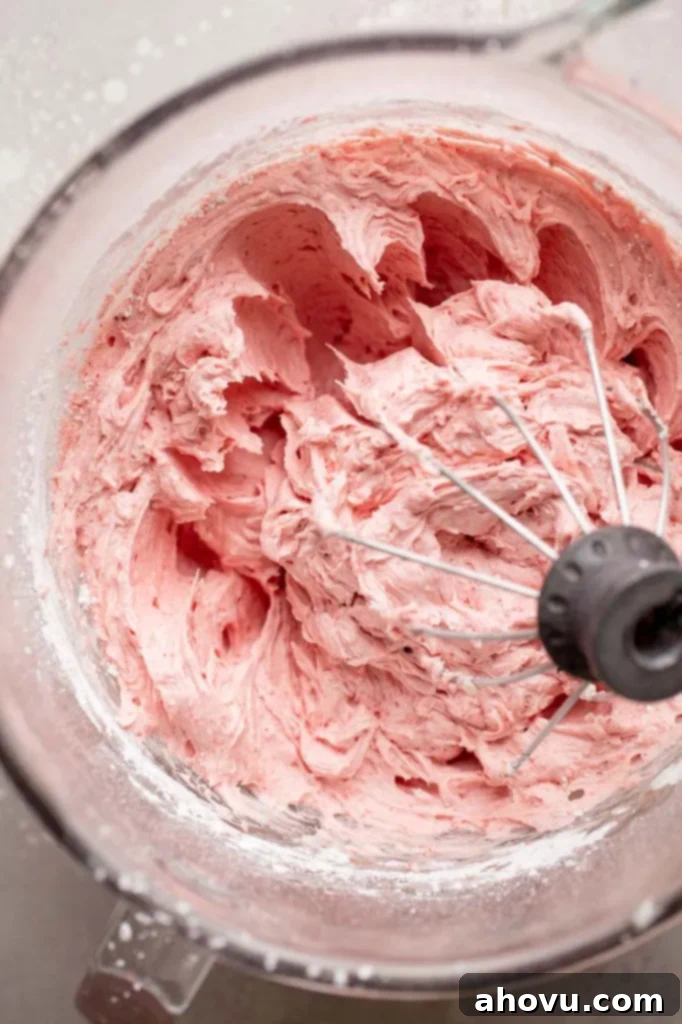 A glass mixing bowl brimming with creamy, pink strawberry buttercream frosting.