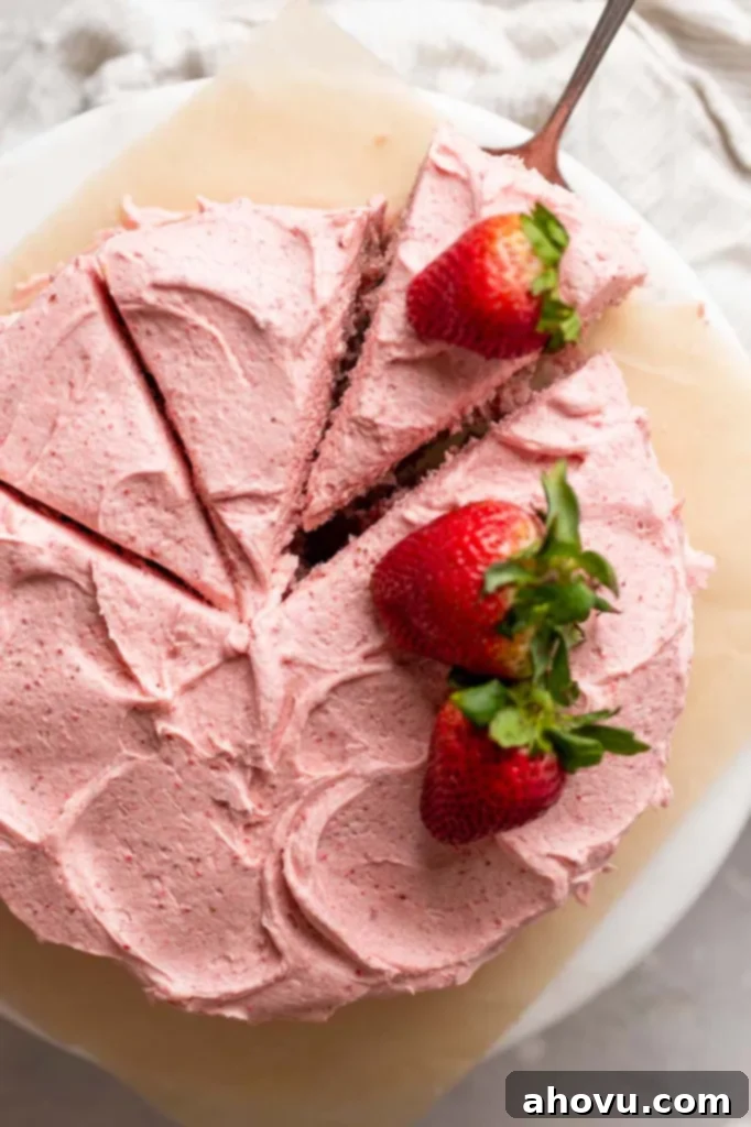 An overhead shot of a freshly baked and frosted strawberry cake, with one perfectly cut slice being removed, revealing the soft interior.