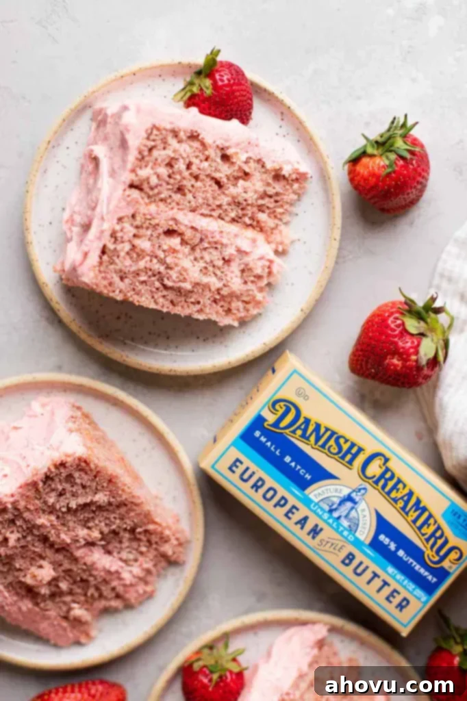 An inviting overhead view of several slices of homemade strawberry cake on white speckled plates, surrounded by a box of Danish Creamery butter and fresh strawberries.