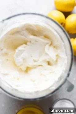 An overhead view of a glass mixing bowl filling with beaten cream cheese.