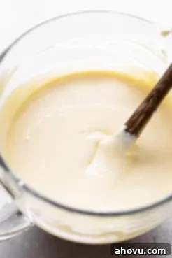 An overhead view of a glass mixing bowl filled with cheesecake filling.