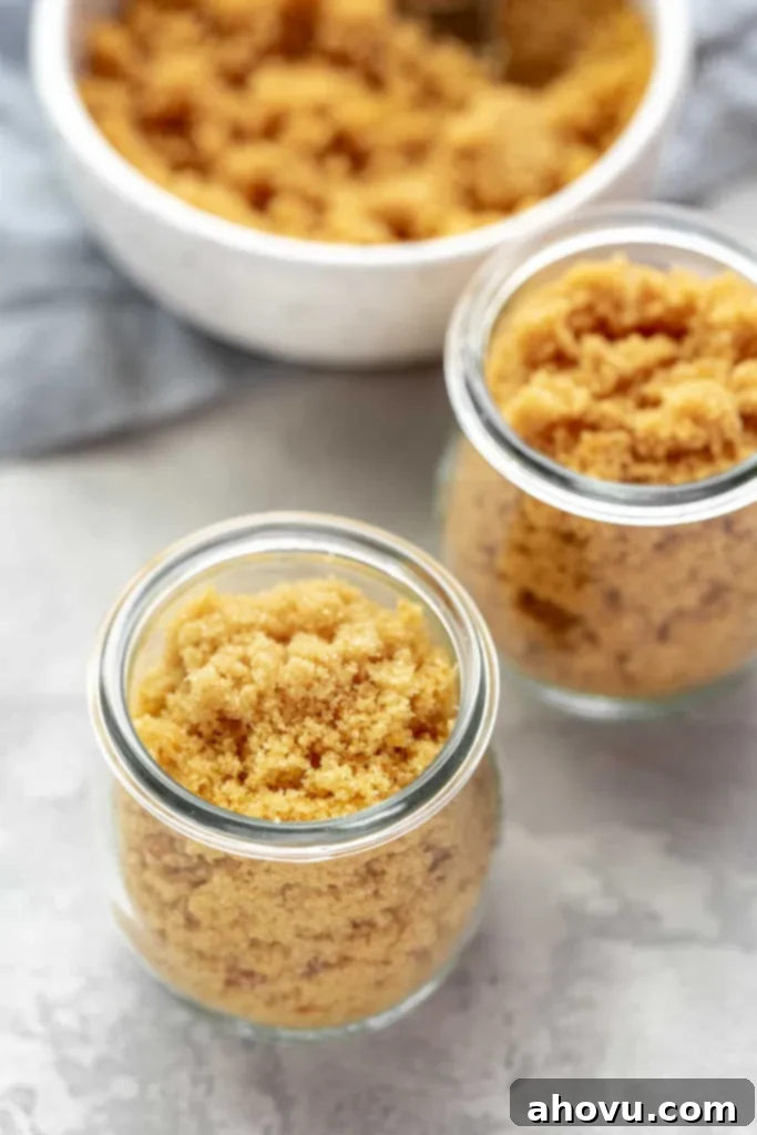 Two glass jars full of a homemade brown sugar substitute. A bowl of brown sugar rests in the background. 