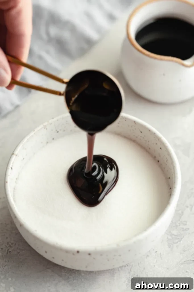 Molasses being poured into a bowl of granulated sugar. A small jug of molasses rests in the background. 